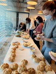 A young woman in a gray sweater, COVID mask and surgical gloves stands beside other women at a long table, assembling sandwiches for Ukrainian refugees.